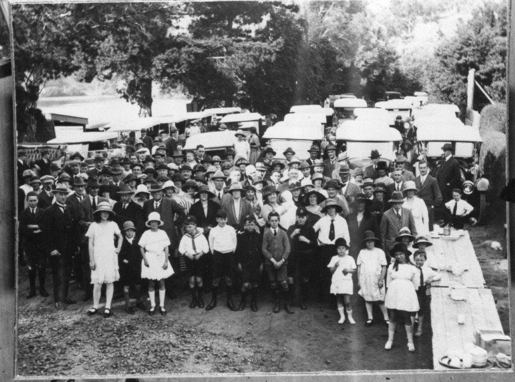 Vintage image of a large group of people standing in front cars